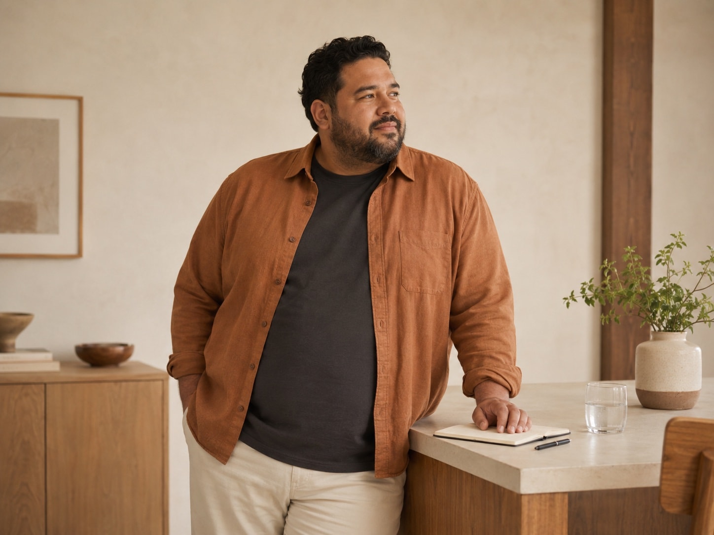 A person standing at a kitchen counter with a notebook, looking toward the window